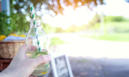 Closeup hand with bottle of lemonade. Drink fresh lemonade on a hot summer day in nature. Place for text.の写真素材