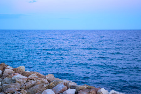 Tranquil coastal view of calm ocean at twilight with rocky foreground creates serene ambianceの写真素材