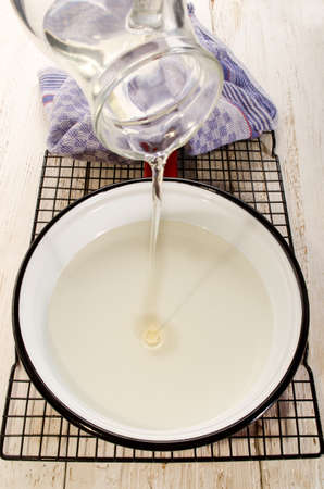 sunflower oil being poured from a glass jug in a red white enamel panの写真素材