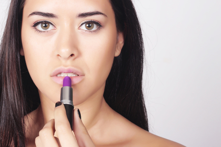 Closeup of young beautiful woman applying lipstick. Beauty makeup caucasian woman isolated over grey background.の写真素材
