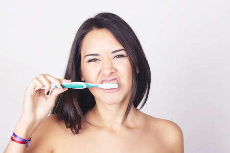 Young beautiful caucasian woman brushing her teeth. Isolated over white background.の写真素材