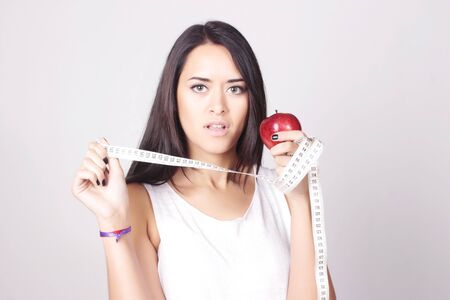 Young caucasian woman holding an apple and measure tape. Fitness and diet concept. Healthy lifestyle.の写真素材