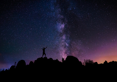 Silhouette of a man standing on top of a hill, with the milky way on the background. Freedom and success concept.の写真素材