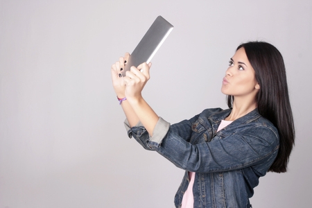 Tablet computer. Young woman holding tablet computer isolated on grey background. Casual caucasian woman taking a selfie.の写真素材