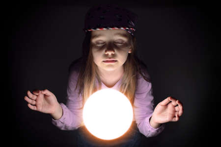 Cute little girl concetrating over a glowing crystal ball, predicting the futureの写真素材