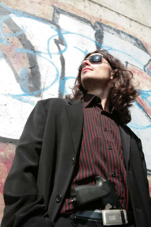 portrait of the young man with gun in black sunglasses in gangster style