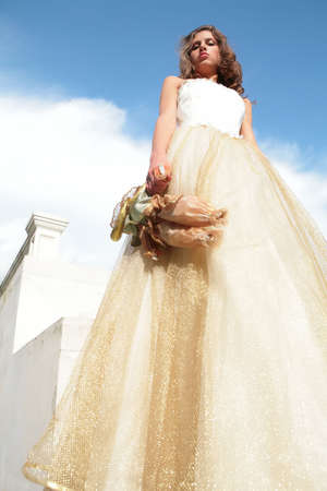 supercilious princess with toy and in white-golden gown on background blue skyの写真素材