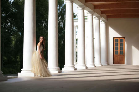 girl in white-golden gown of the bride amongst colonnades of the old-time buildingの写真素材