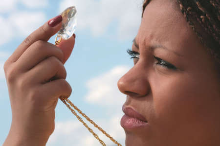 african girl keeps finger large diamond and looks through it on lightの写真素材