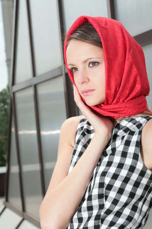 serious young beautiful girl in red kerchief and hand near faceの写真素材