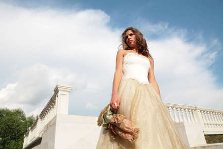 horizontal portrait of the bride in white-golden gown on background blue sky with cloudsの写真素材