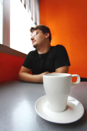 single man looks to window and coffee cup stand on the tableの写真素材