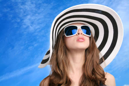 beautiful girl in striped hat and sunglasses on background blue skyの写真素材