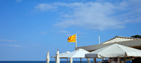 White umbrellas and the flag of Catalunya under a blue sky on the beachの写真素材