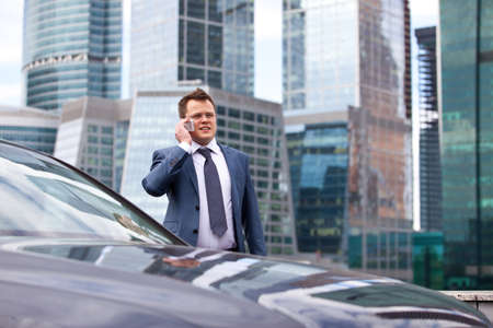 successful businessman talking on the phone near the car, on the background of office buildingsの写真素材
