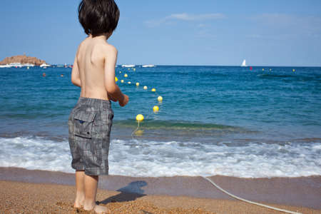 boy standing on the shore looking at the blue seaの写真素材