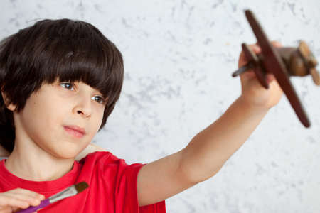 portrait of a boy in a red shirt with a wooden plane and brushの写真素材