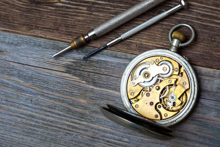 antique clock with an open mechanism and two screwdrivers on a textured background