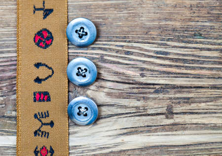 vintage tape with embroidered ornaments andÂ three old button on a textured surface aged boardsの写真素材