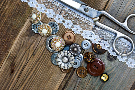 vintage buttons, lace, and a dressmaker scissors on a textured surface of old boardsの写真素材