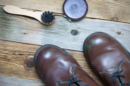 Still life with brown boots, shoe polish and shoe brush on the old boards
