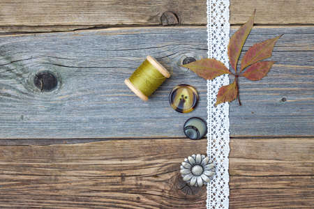 still life with lace ribbon, vintage buttons, spools of thread and dry leavesÂ on the surface of...