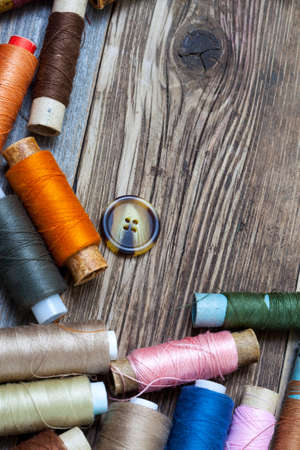 Vintage spools with multi colored threads and old button on old tailoring table