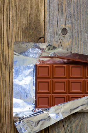 milk chocolate in a foil on a background of old boardsの写真素材