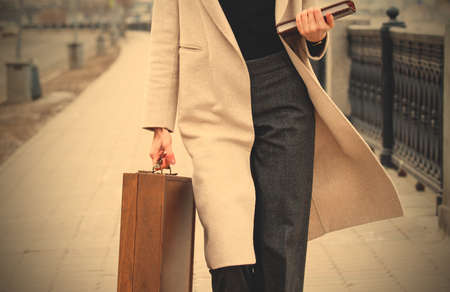 woman in a light coat, with a wooden case and a book in his hands outdoors. close-up.の写真素材