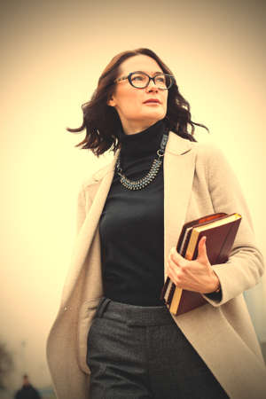 beautiful dark-haired middle-aged woman in a bright coat and with books in their hands.  image filter retro styleの写真素材