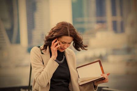 beautiful middle-aged woman in a bright coat and with a notebook in his hand talking on the mobile phone. image of a business woman.  image filter retro styleの写真素材