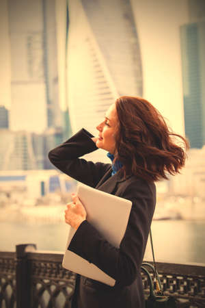 smiling woman with a laptop on the background of urban office buildings. business woman outside office.  image filter retro styleの写真素材