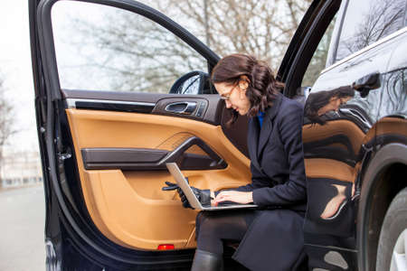 dark haired woman with a laptop sit on the step of the car with the door openの写真素材