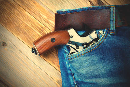 silver revolver nagant with brown handle  in the pocket of old blue jeans. close up.の写真素材