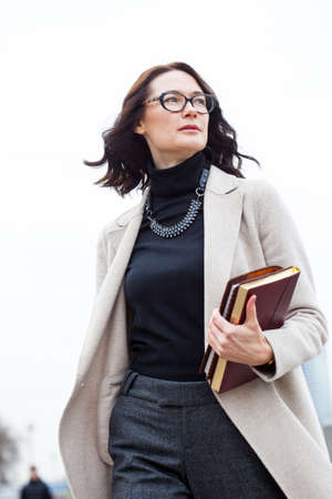 beautiful dark-haired middle-aged woman in a bright coat and with books in their handsの写真素材