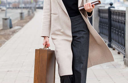 woman in a light coat, with a wooden case and a book in his hands outdoors. close-upの写真素材