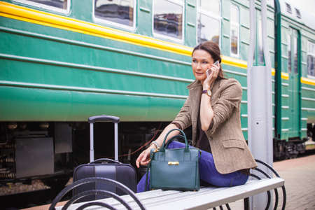 beautiful woman talking on a cell and wait for the train to go on a retro travel by railwayの写真素材