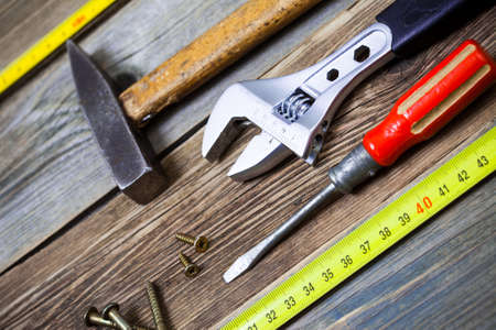 old screwdriver, screws, monkey wrench, vintage hammer and tape-measure on the boards of the old workbenchの写真素材