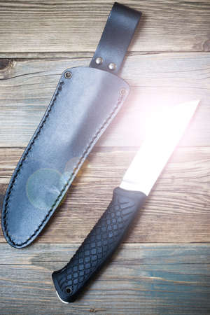 shiny hunting knife and leather scabbard on a textured surface of old wooden planksの写真素材