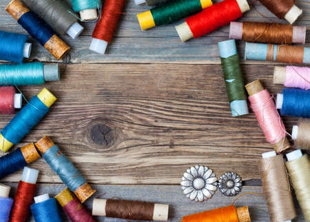 vintage reels of varicolored thread and old flower buttons on the textured surface of the ancient...