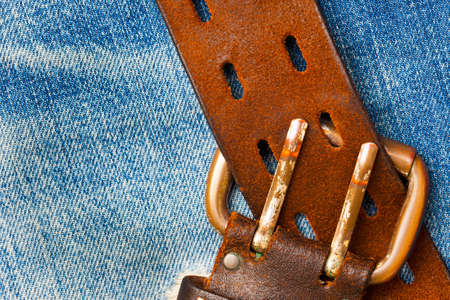 unfastened old leather belt with vintage buckles on the jeans background