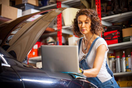 pretty woman mechanic diagnoses the car engine works. preparing to travel. fashion. technologiesの写真素材