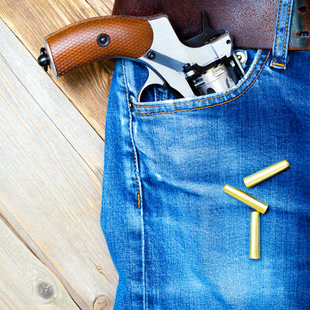 old gun with brown handle in the pocket of vintage blue jeans, close upの写真素材