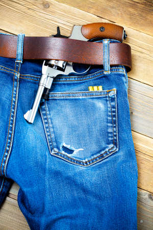 silver gun under a leather belt of blue jeans