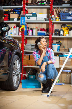 beautiful female mechanic in an auto repair shop talking on mobileの写真素材