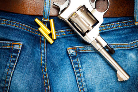 revolver with cartridges on old blue jeans with leather belt, close upの写真素材