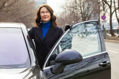 Smiling beautiful business woman near car with the open door