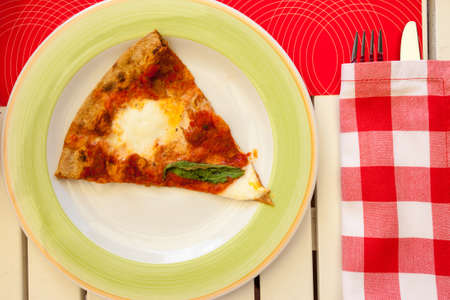 slice of pizza Margherita on a plate with a napkin, knife and fork in a restaurant