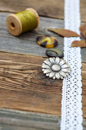 vintage buttons with lace tape and spools of thread on aged wooden surface. Still life. Focus located on button flowerの写真素材