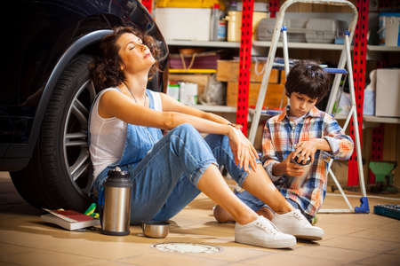 resting mechanic woman and boy with thermos in an auto repair workshopの写真素材